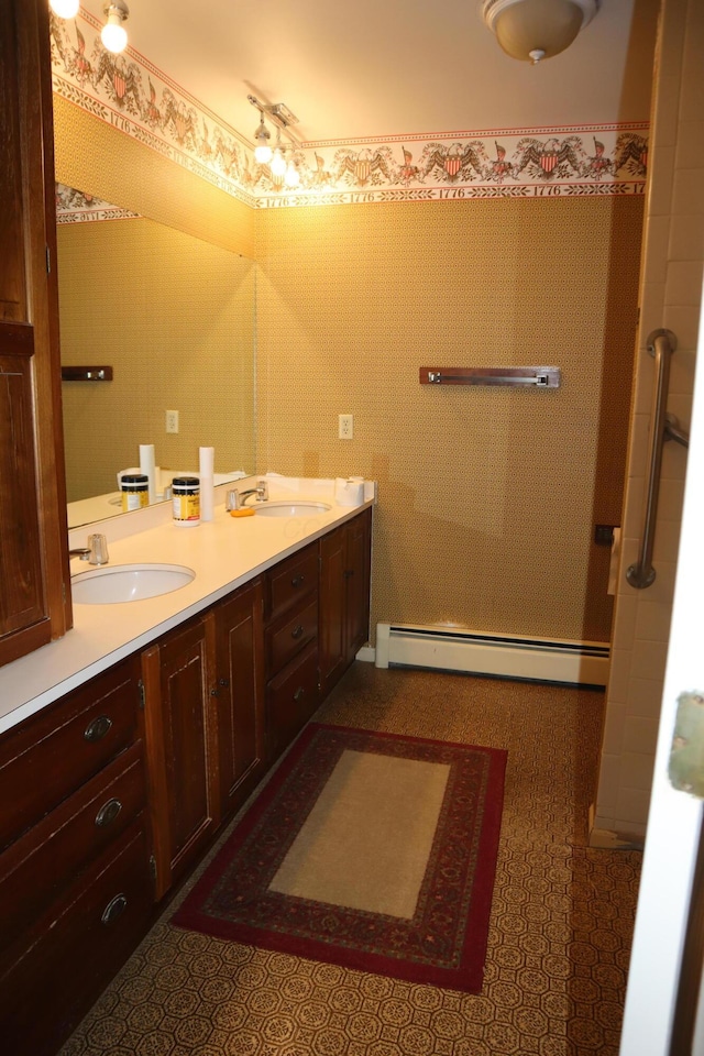 bathroom featuring double vanity, baseboard heating, wallpapered walls, and a sink