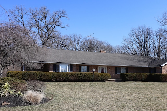 ranch-style home with brick siding, a chimney, and a front yard