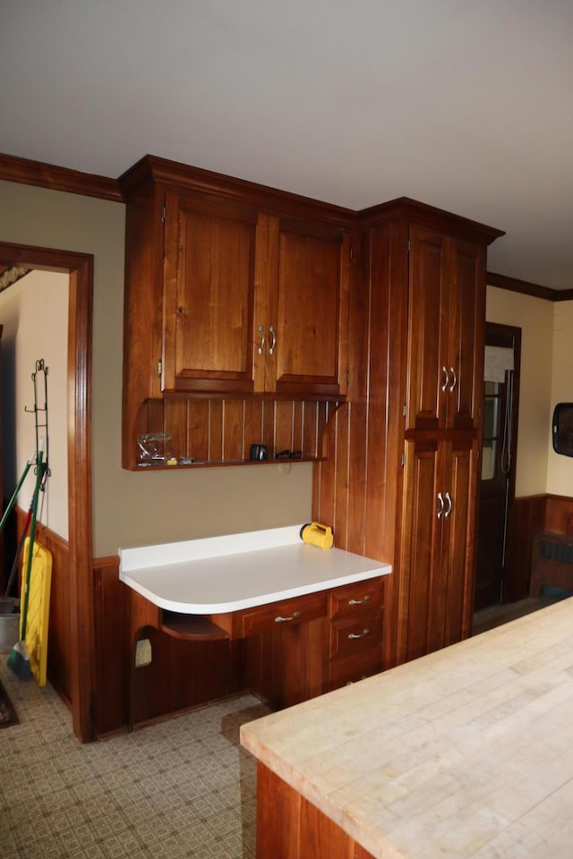 kitchen with light countertops, wooden walls, ornamental molding, and wainscoting