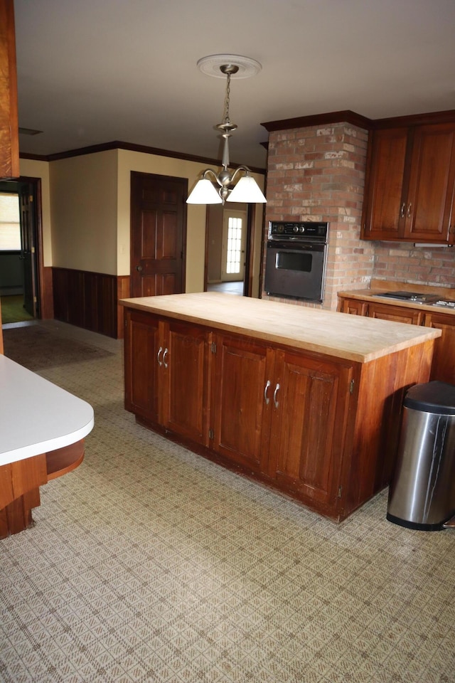 kitchen with wainscoting, oven, light countertops, pendant lighting, and crown molding