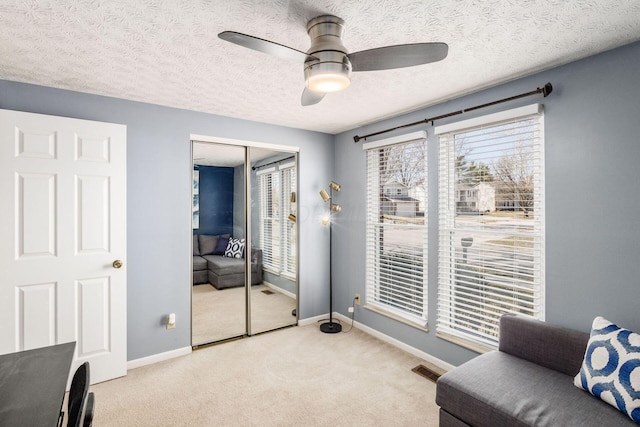 living area with visible vents, baseboards, carpet, a textured ceiling, and a ceiling fan