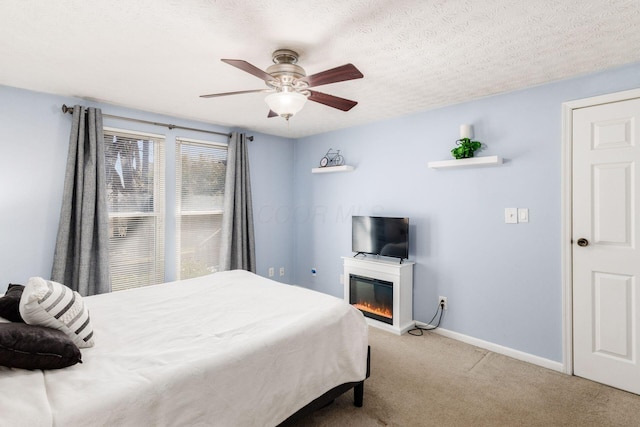 carpeted bedroom with a glass covered fireplace, ceiling fan, a textured ceiling, and baseboards