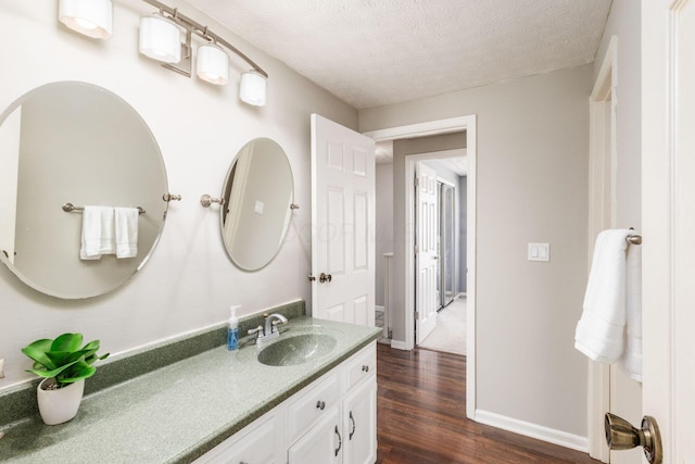 bathroom featuring a textured ceiling, vanity, baseboards, and wood finished floors