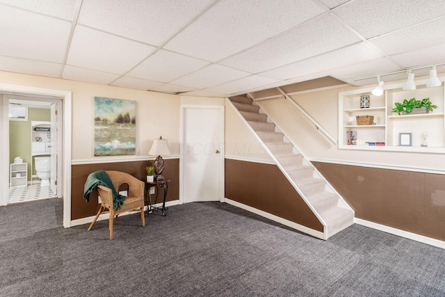 sitting room with built in features, carpet, a drop ceiling, stairs, and rail lighting