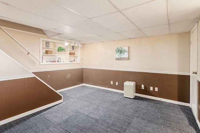 below grade area with built in features, baseboards, a drop ceiling, rail lighting, and carpet flooring