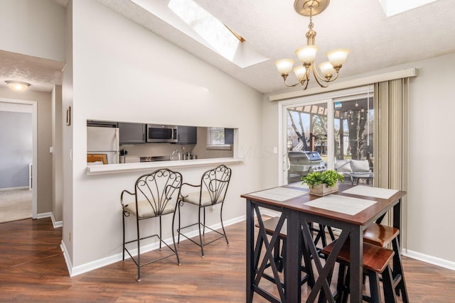 dining space with dark wood finished floors, vaulted ceiling with skylight, a textured ceiling, and baseboards