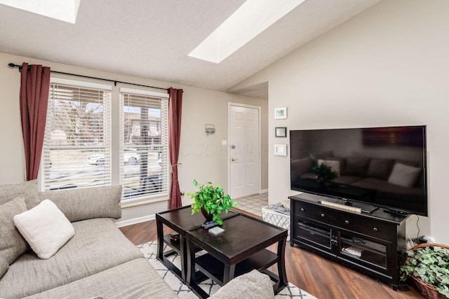 living room featuring lofted ceiling with skylight, baseboards, and wood finished floors