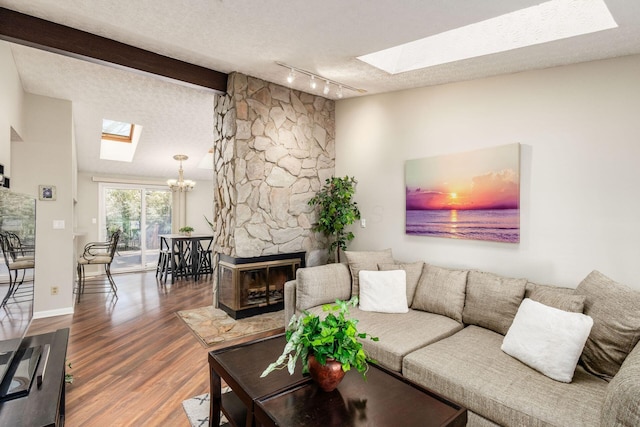 living room featuring wood finished floors, baseboards, vaulted ceiling with skylight, a fireplace, and a textured ceiling