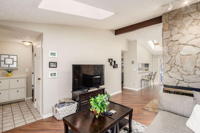 living area with lofted ceiling with skylight, wood finished floors, baseboards, and a textured ceiling