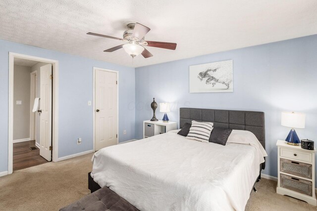 carpeted bedroom with ceiling fan, a textured ceiling, ensuite bathroom, and baseboards