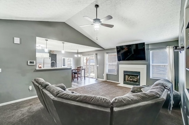 living room featuring baseboards, carpet, vaulted ceiling, a textured ceiling, and a ceiling fan