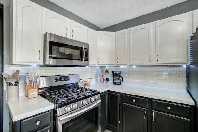 kitchen with a textured ceiling, dark cabinetry, stainless steel appliances, white cabinets, and decorative backsplash