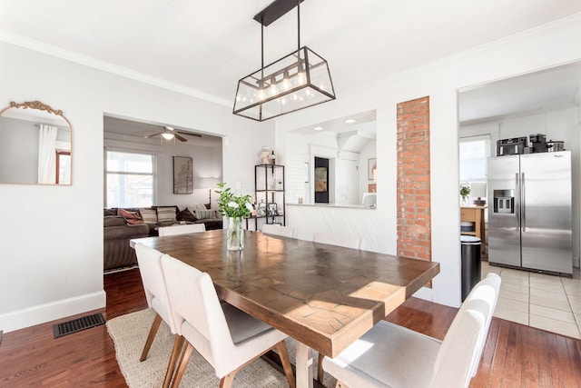 dining space with baseboards, visible vents, light wood-style flooring, ceiling fan, and ornamental molding