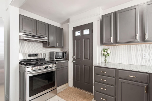 kitchen featuring under cabinet range hood, light tile patterned floors, light stone counters, decorative backsplash, and stainless steel appliances