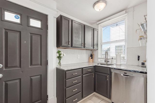 kitchen featuring a sink, backsplash, stainless steel dishwasher, light tile patterned flooring, and light stone countertops