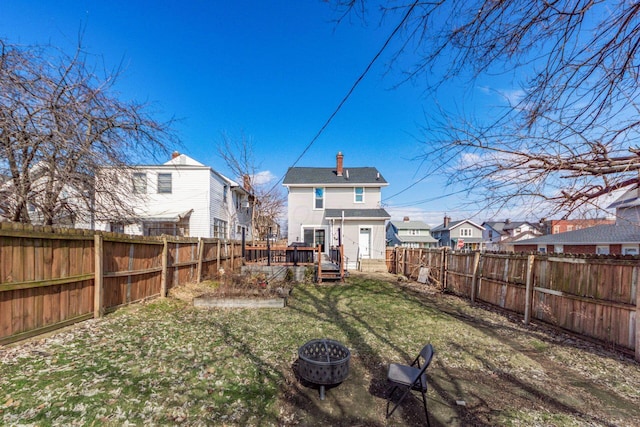 back of property featuring an outdoor fire pit, a lawn, a chimney, a deck, and a fenced backyard