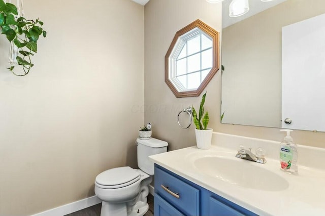 half bathroom with vanity, toilet, and baseboards