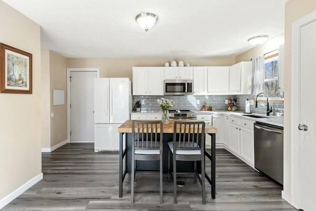 kitchen featuring a sink, tasteful backsplash, appliances with stainless steel finishes, white cabinets, and baseboards