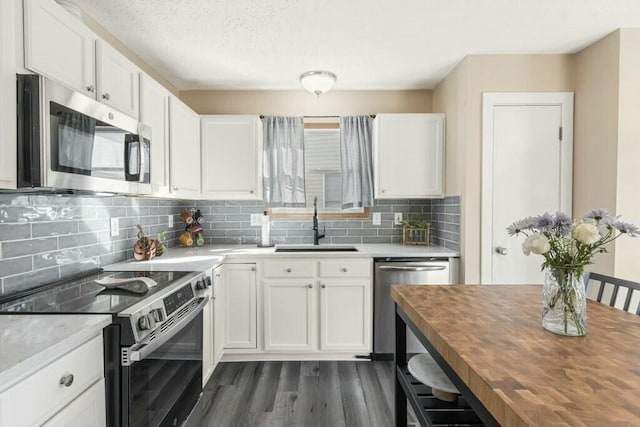 kitchen with a sink, appliances with stainless steel finishes, white cabinets, butcher block counters, and decorative backsplash