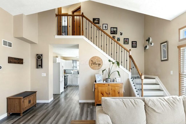 living area featuring visible vents, baseboards, stairs, a towering ceiling, and dark wood-style flooring