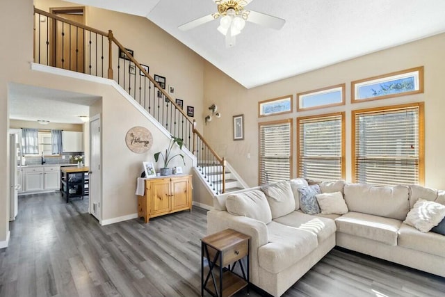 living area with stairway, a ceiling fan, wood finished floors, baseboards, and high vaulted ceiling