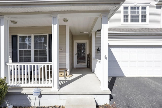 property entrance with a garage, covered porch, and aphalt driveway