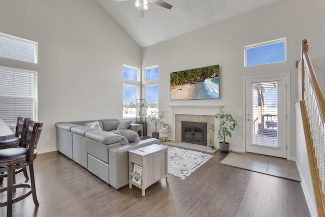 living area with a glass covered fireplace, wood finished floors, baseboards, and high vaulted ceiling