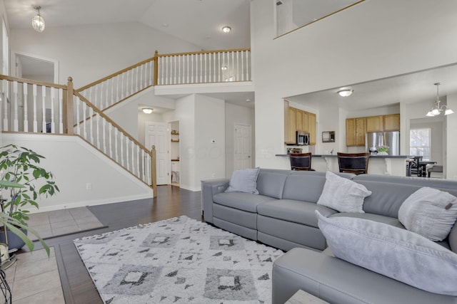 living room with stairway, wood finished floors, baseboards, high vaulted ceiling, and a notable chandelier