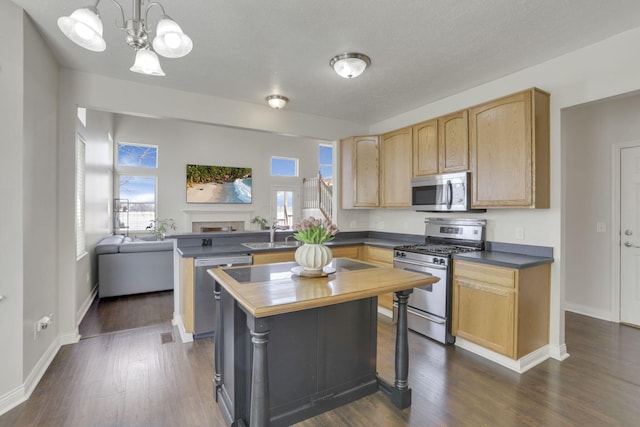 kitchen featuring light brown cabinets, a peninsula, dark wood-style flooring, a sink, and stainless steel appliances