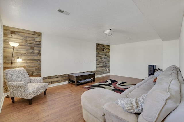 living area featuring visible vents, wood finished floors, a textured ceiling, and wood walls