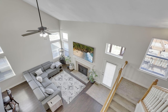 living area with high vaulted ceiling, wood finished floors, a fireplace, baseboards, and ceiling fan