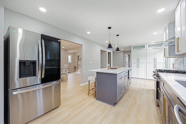 kitchen with under cabinet range hood, backsplash, stainless steel appliances, and light wood-type flooring