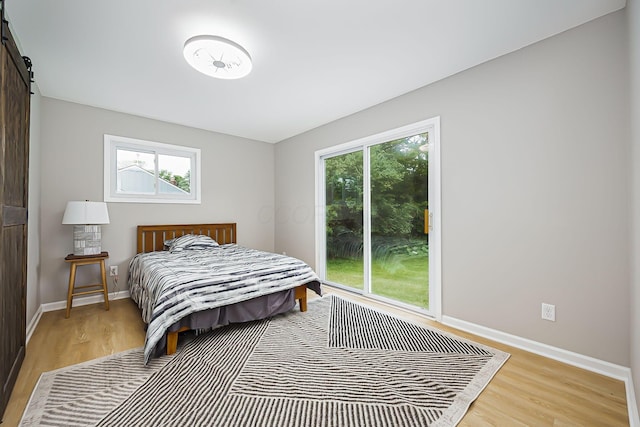 bedroom featuring access to exterior, light wood-style flooring, baseboards, and a barn door