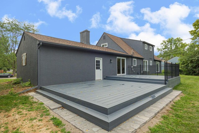 rear view of house with a chimney, stucco siding, a wooden deck, and a lawn