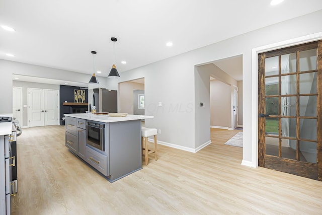 kitchen with gray cabinetry, light wood-type flooring, light countertops, stainless steel appliances, and a kitchen island with sink