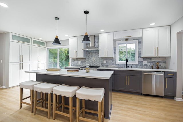 kitchen with a sink, a breakfast bar area, wall chimney range hood, and stainless steel dishwasher