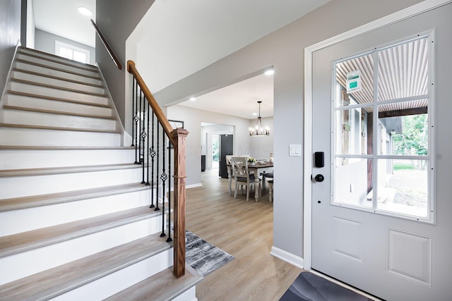 foyer entrance with a notable chandelier, stairway, baseboards, and light wood-style floors