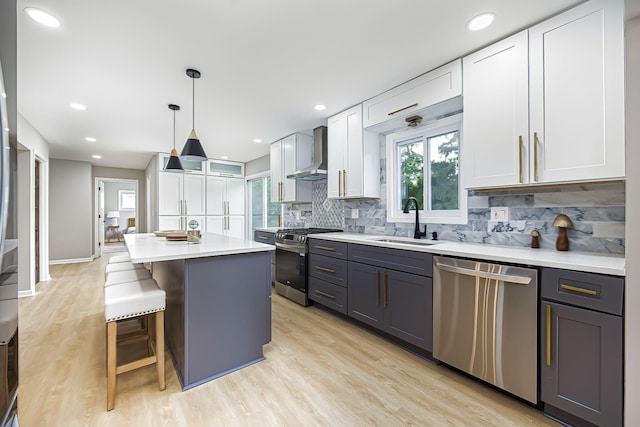 kitchen with a sink, backsplash, stainless steel appliances, wall chimney exhaust hood, and white cabinets