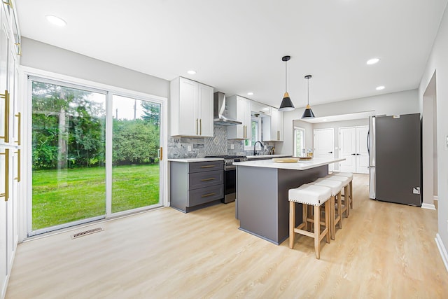 kitchen with visible vents, a kitchen island, wall chimney range hood, light countertops, and stainless steel appliances