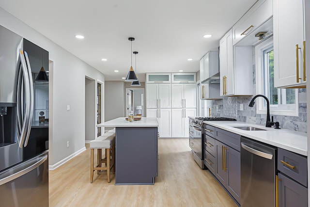 kitchen with a kitchen bar, light wood-style flooring, a sink, tasteful backsplash, and appliances with stainless steel finishes