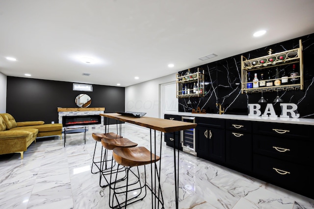 bar with a premium fireplace, wet bar, recessed lighting, wine cooler, and marble finish floor