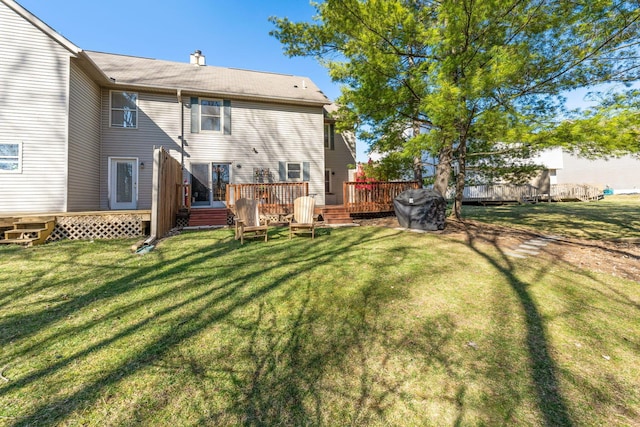 rear view of house featuring a lawn, a chimney, and a wooden deck