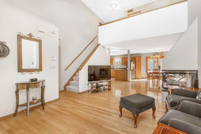 living area with stairway, a high ceiling, an inviting chandelier, light wood finished floors, and baseboards