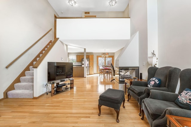 living area featuring light wood finished floors, baseboards, a chandelier, stairs, and a towering ceiling