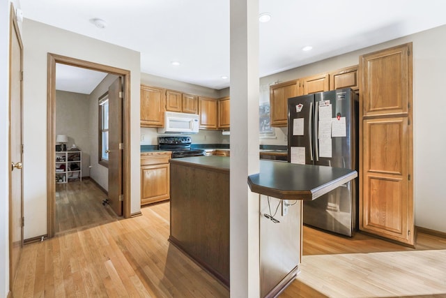 kitchen with stove, white microwave, light wood-style floors, and freestanding refrigerator