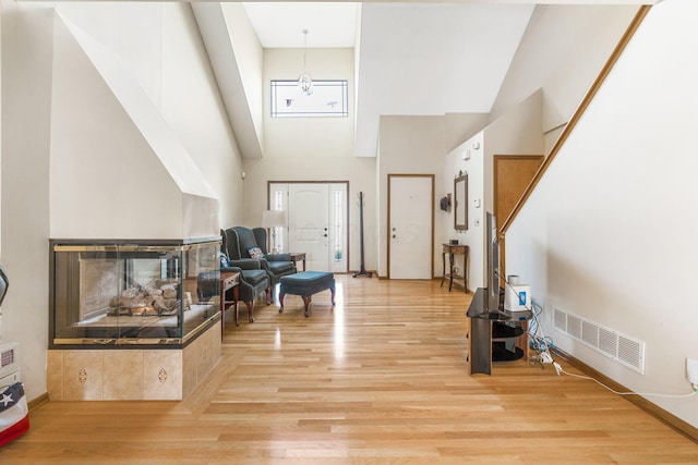 entrance foyer with a multi sided fireplace, visible vents, light wood finished floors, and a towering ceiling