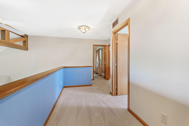 hallway with visible vents, baseboards, and light colored carpet