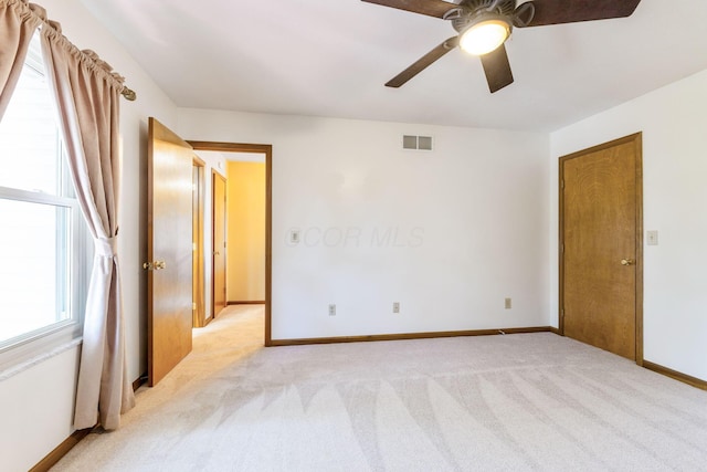 unfurnished bedroom featuring multiple windows, light colored carpet, visible vents, and baseboards