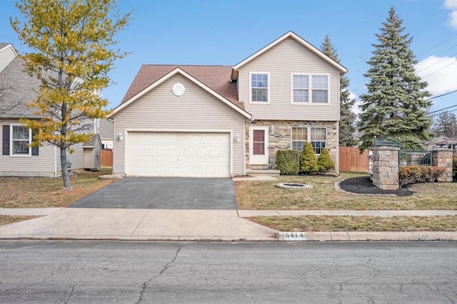 view of front facade with a front yard, fence, driveway, a garage, and stone siding