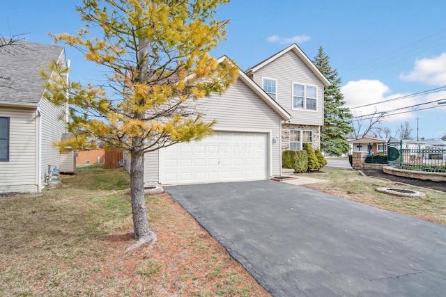 traditional-style home featuring aphalt driveway, an attached garage, fence, and a front yard